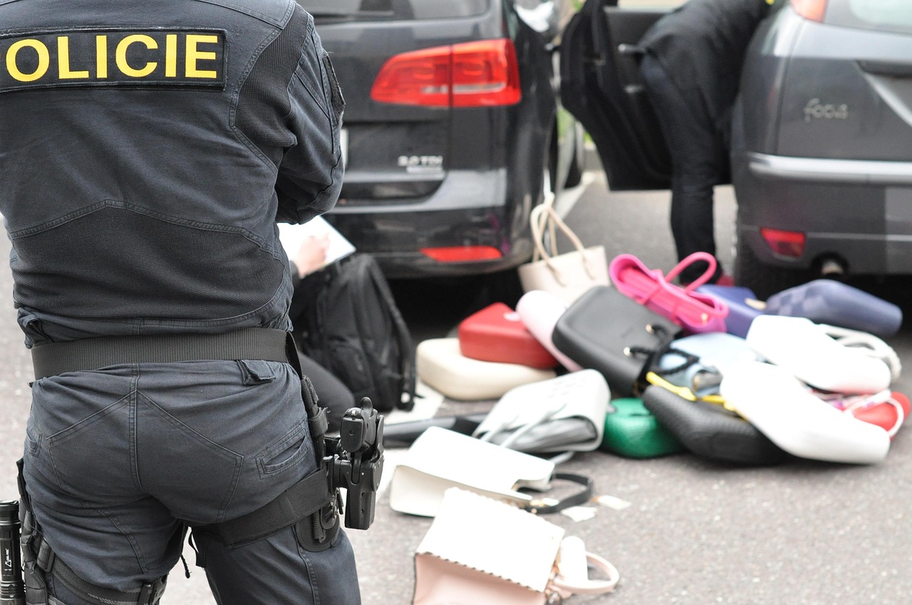 A police officer standing in front of a car and a pile of counterfeit bags lying on the ground