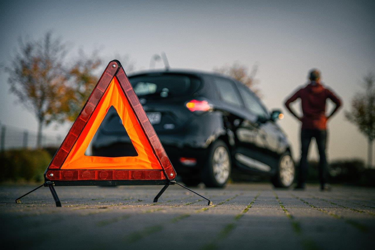 A warning triangle placed on the road, in front of a stopped car and its driver