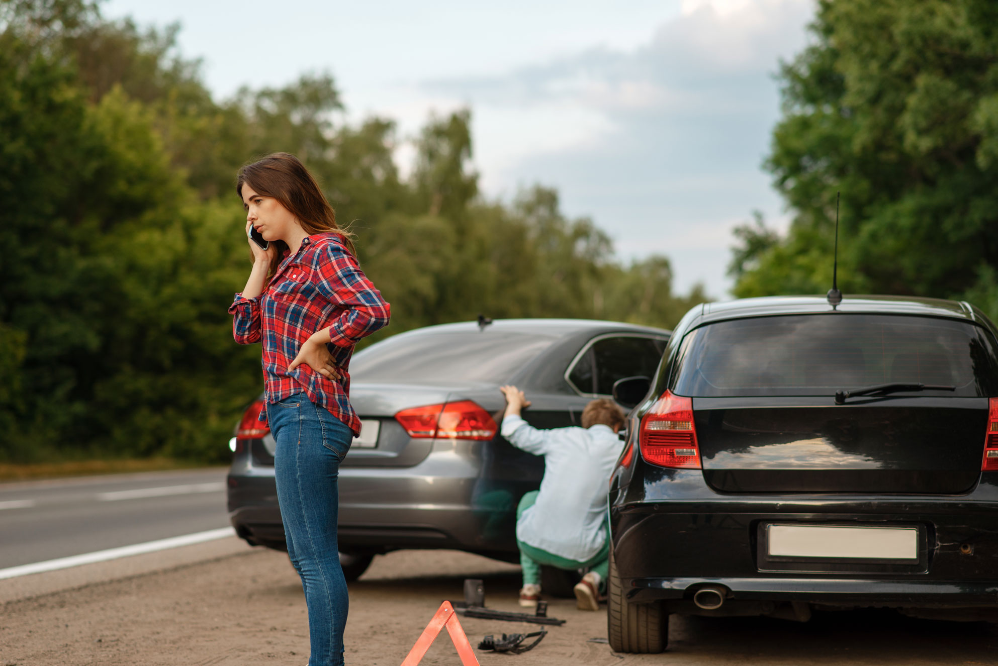 A woman on the phone while a man inspects the two collided cars